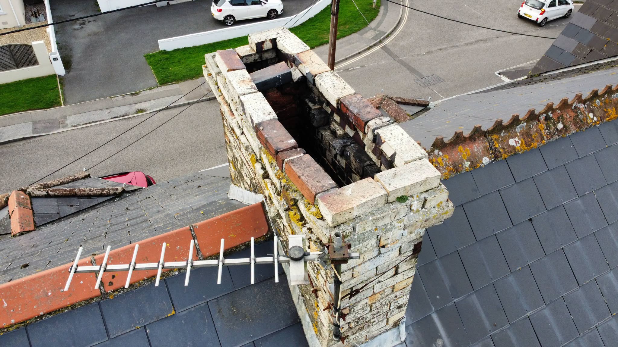 Old chimney stack seen from above, pots off and flues open, beside a TV aerial on a slate roof