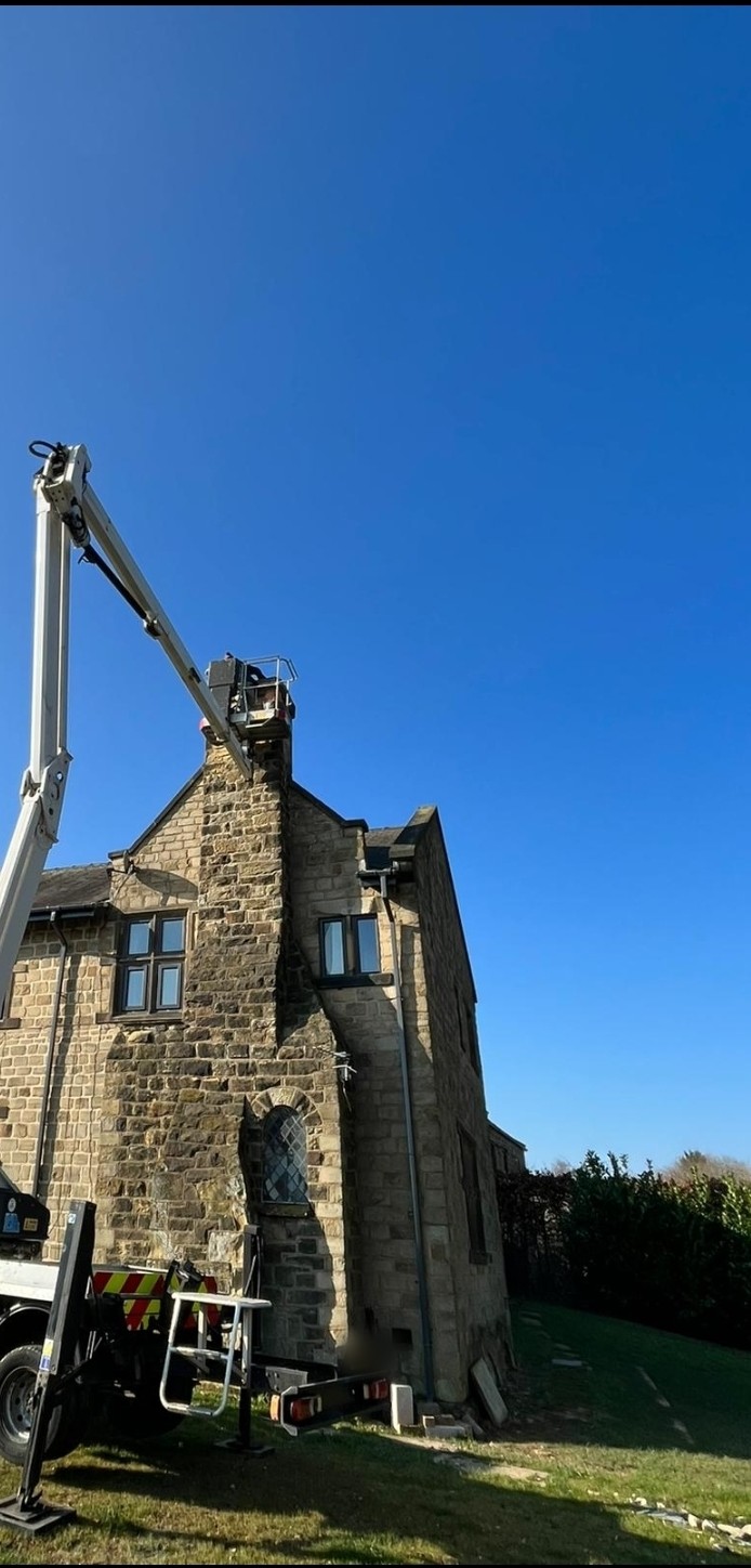 An access platform raised to the chimney of a tall stone house under a blue sky